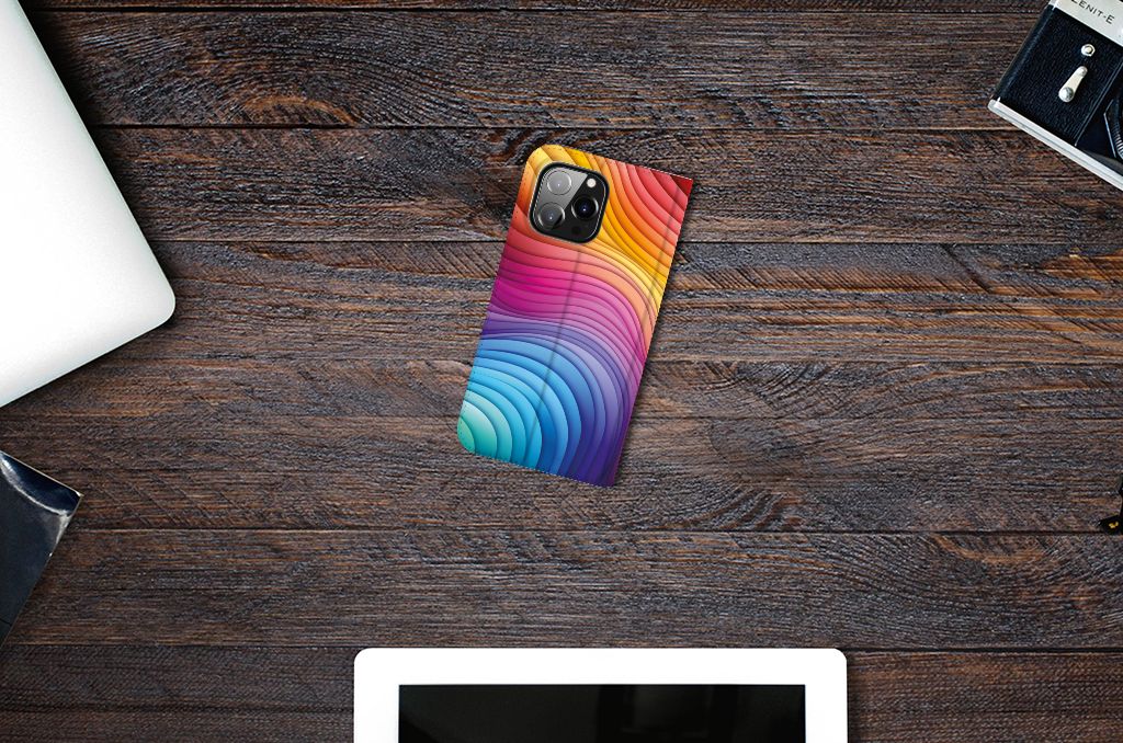 Stand Case voor iPhone 14 Pro Max Regenboog op een houten bureau met andere apparaten.