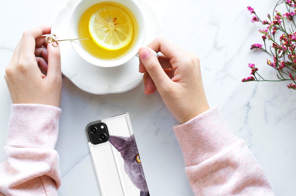 Een vrouw met een iPhone 13 Mini Hoesje maken Kat en een kopje thee met citroen.
