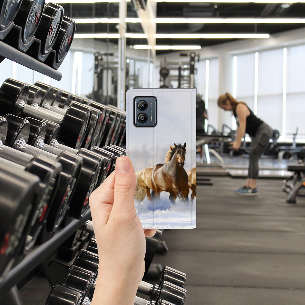 Motorola Moto G53 Hoesje maken Paarden in gebruik in een sportschool met gewichten op de achtergrond.