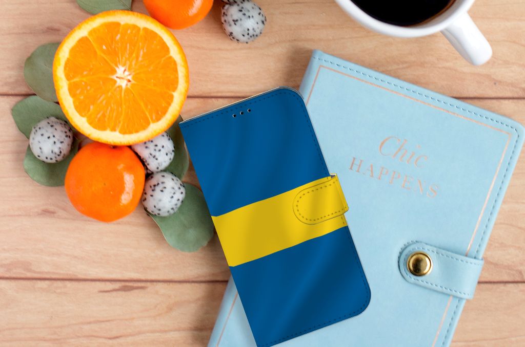iPhone 14 Plus Bookstyle Case Zweden met blauwe en gele kleuren, gelegen op een houten ondergrond met fruit en een notitieboek.