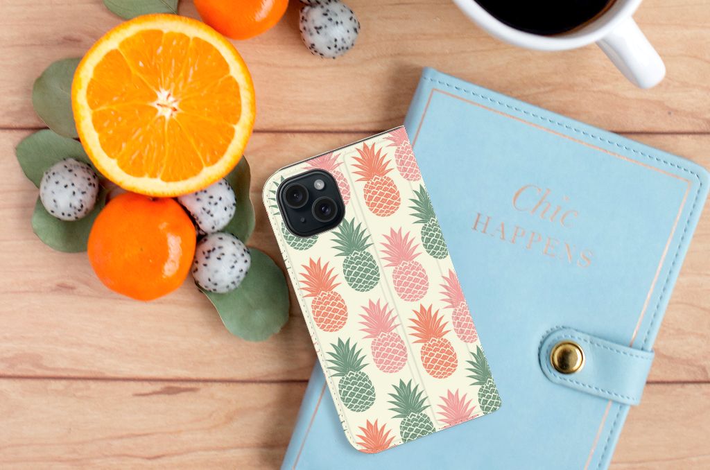 iPhone 15 Flip Style Cover Ananas met kleurrijke ananasprint op een houten tafel met fruit en notitieboek