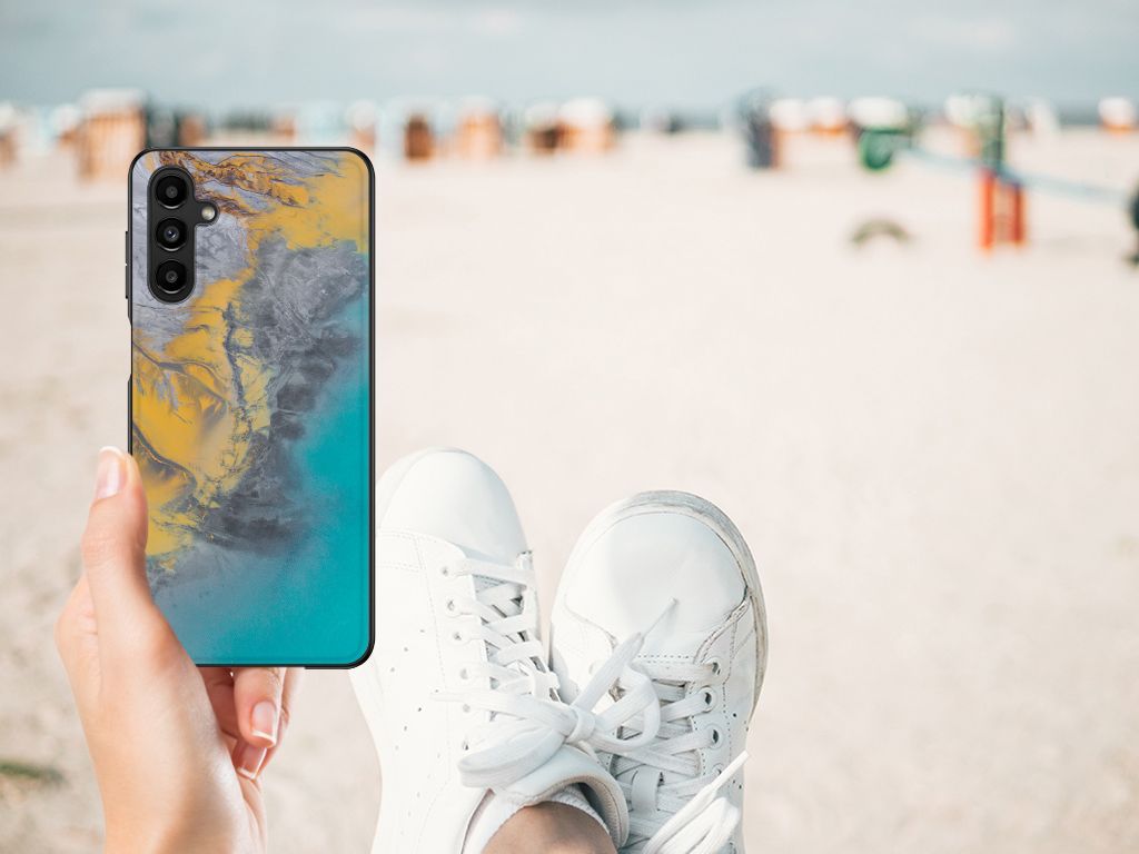 Samsung Galaxy A14 5G Marmeren Print Telefoonhoesje Marble Blue Gold in handen op het strand met sneakers.