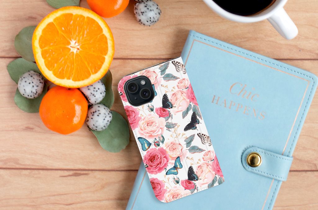 iPhone 15 Smart Cover Butterfly Roses met bloemen en vlinders, liggend naast fruit en een notitieboekje.