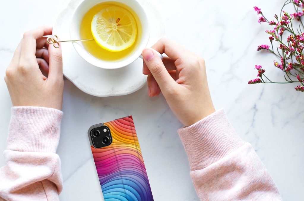 Stand Case voor iPhone 13 Mini Regenboog met kleurrijk design op een tafel naast een kopje thee.