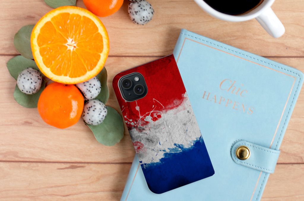 iPhone 15 Standcase Nederland met een decoratief ontwerp in de kleuren van de Nederlandse vlag, omgeven door fruit en een notitieboek.