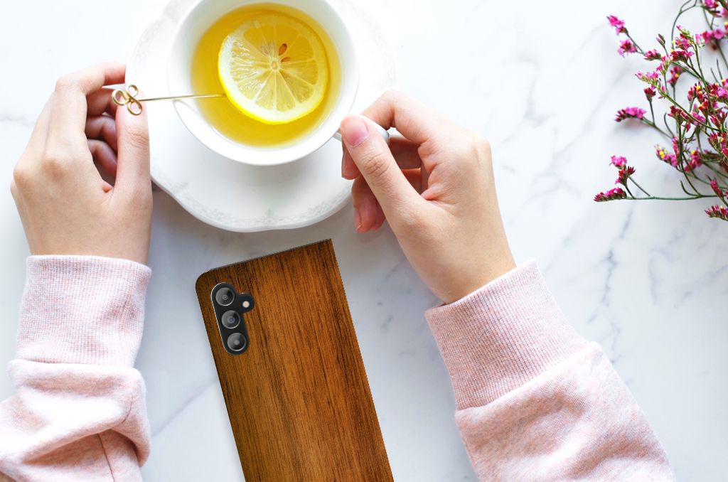 Samsung Galaxy A14 5G Book Wallet Case Donker Hout met een hand die een kopje thee vasthoudt.