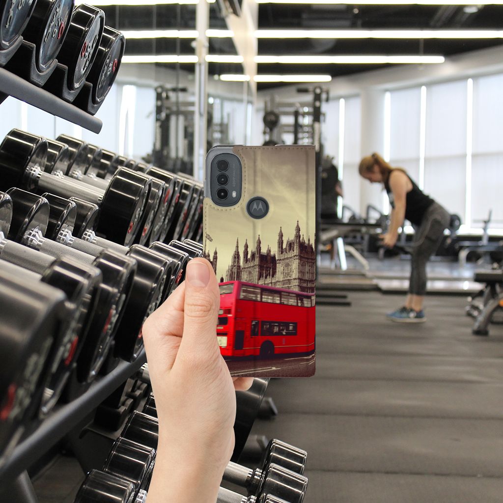 Motorola Moto E20 Book Cover Londen hand met telefoon in sportschool uitzicht met rode bus en gym apparatuur