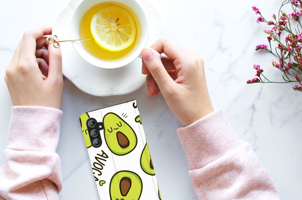 Samsung Galaxy A14 4G Magnet Case Avocado Singing design on phone beside a cup of tea with lemon.