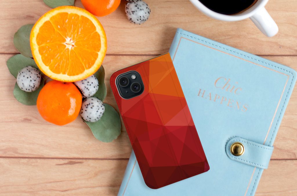 Stand Case voor iPhone 15 Polygon Red met geometrisch design, gelegen naast fruit en een notitieboekje.