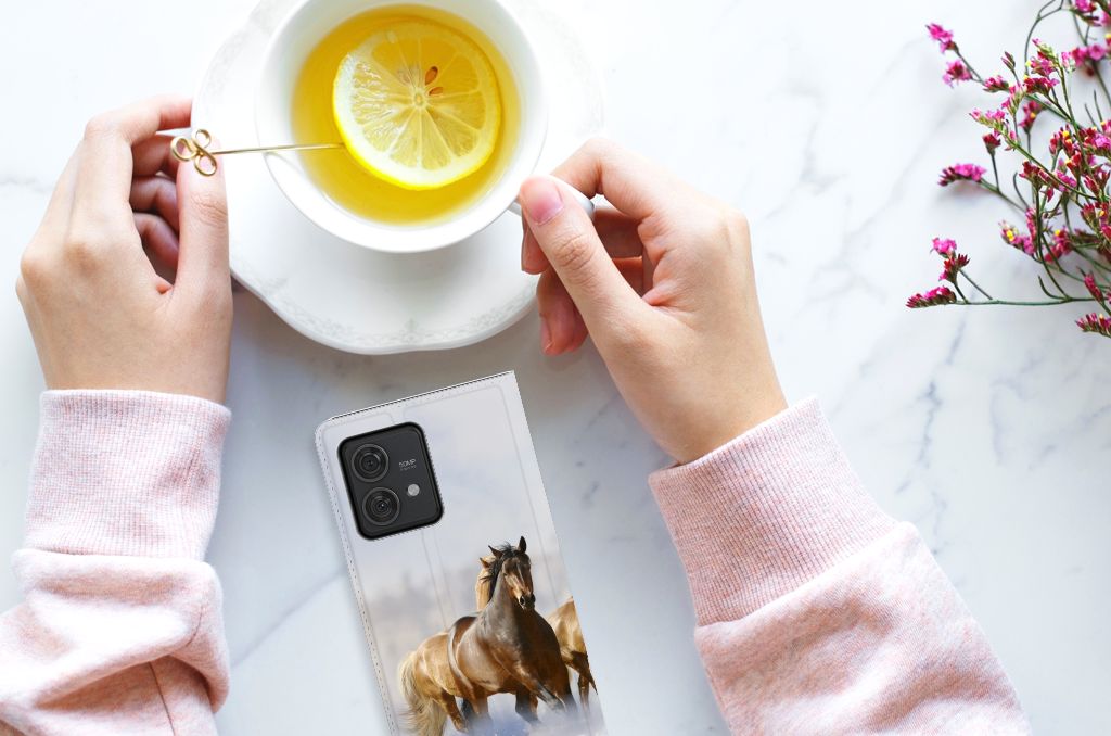Hand holding a Motorola Edge 40 Neo Hoesje maken Paarden next to a cup of lemon tea.