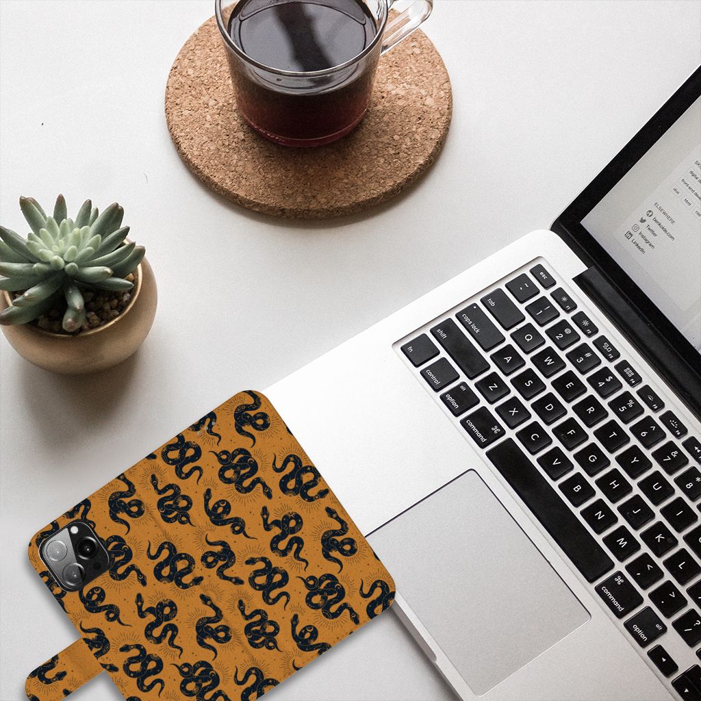 Telefoonhoesje met Pasjes voor iPhone 13 Pro Max Snakes ligt op een bureau naast een laptop en een plant.