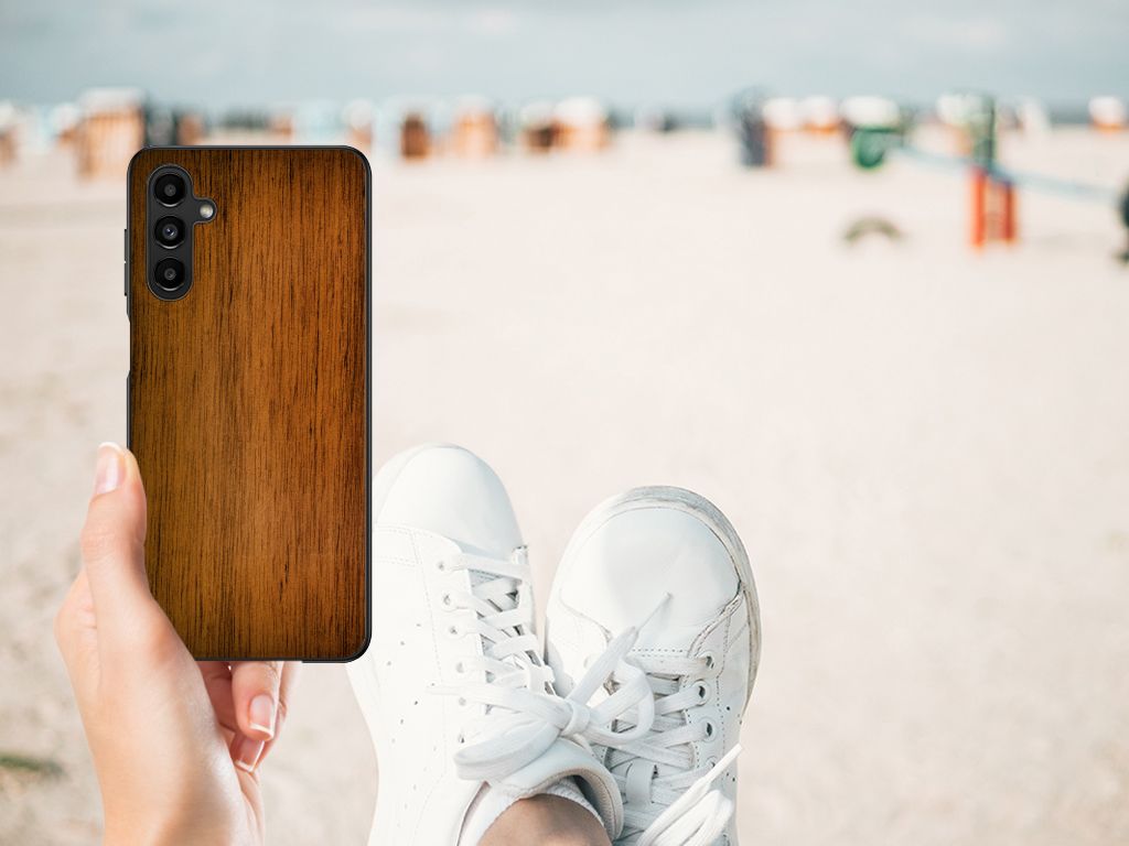 Samsung Galaxy A14 5G Houten Print Telefoonhoesje Donker Hout met een houten afwerking in hand, sneakers op het strand.