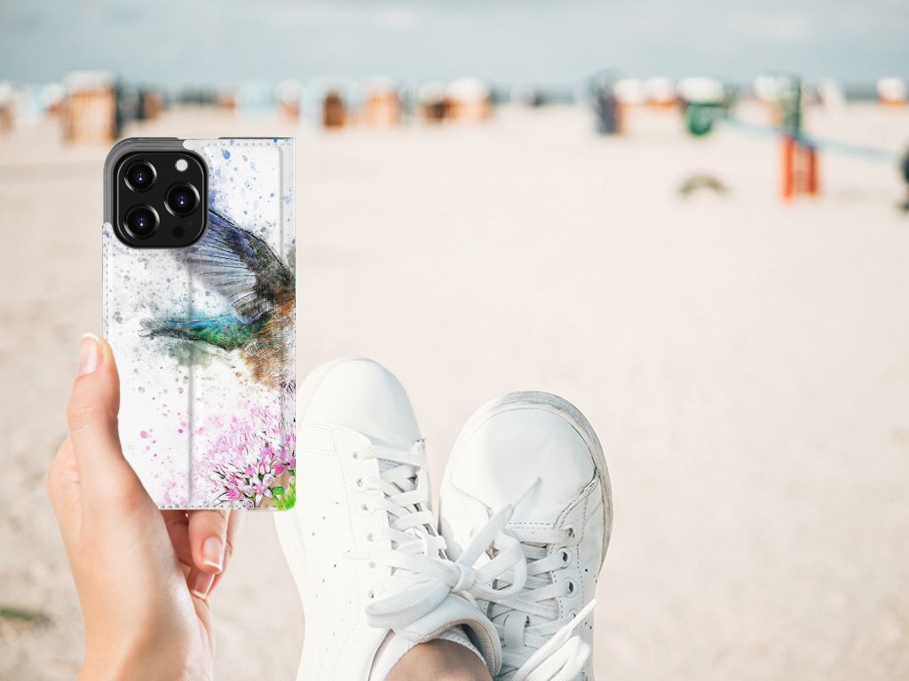 Bookcase iPhone 13 Pro Vogel met kleurrijk design op een strand, hand met sneakers in beeld.