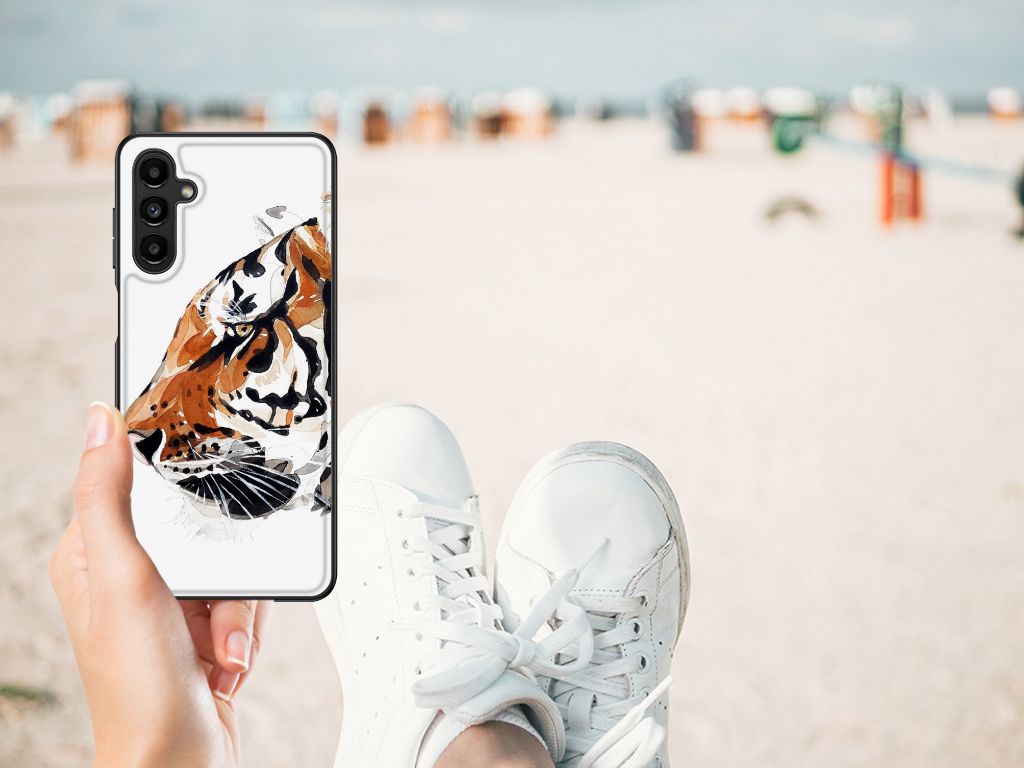 Hand holding a Kleurrijke Telefoonhoesje Samsung Galaxy A14 5G Watercolor Tiger on a beach with sneakers in view.
