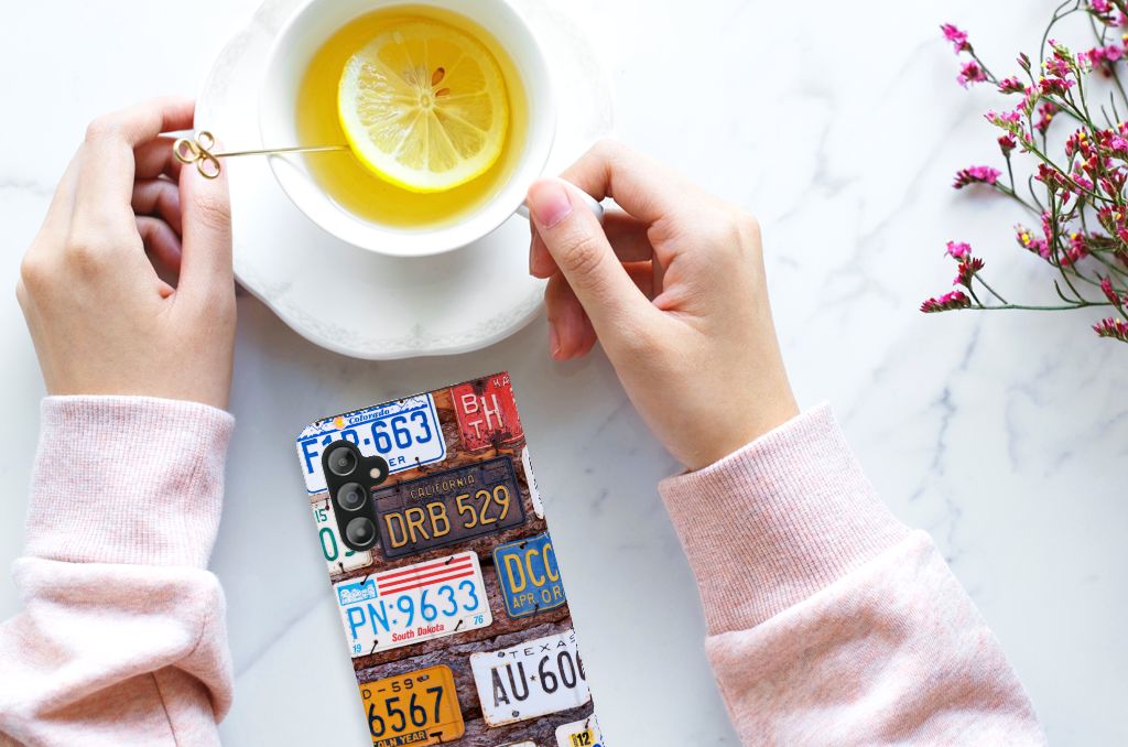 Samsung Galaxy A14 4G Stand Case Kentekenplaten met Amerikaanse kentekenplaten in hand naast een kopje thee.