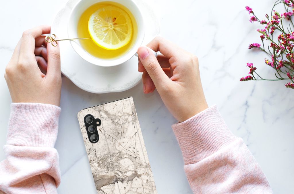 Vrouwelijke handen met een Samsung Galaxy A14 4G Standcase Marmer Beige terwijl ze thee drinkt.