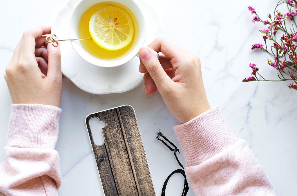 Handen met een Samsung Galaxy A14 5G Stevig Telefoonhoesje Steigerhout en een kopje thee met citroen.