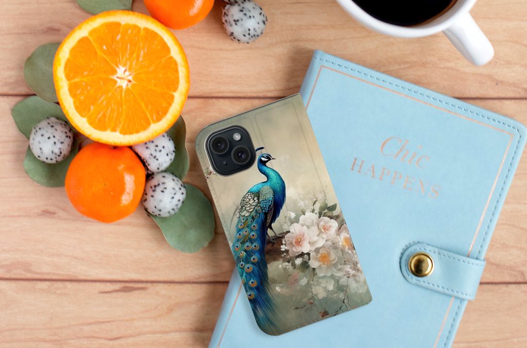 Hoesje maken voor iPhone 15 Vintage Pauwen met een kleurrijke pauwenillustratie, omringd door fruit en een notitieboek.