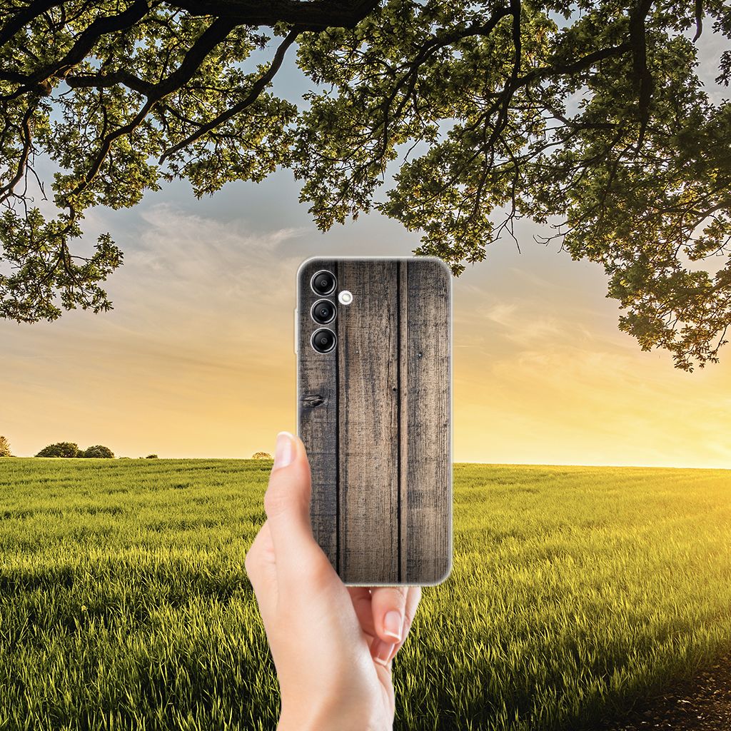 Samsung Galaxy A14 5G Bumper Hoesje Steigerhout met een houten afwerking, gehouden tegen een achtergrond van natuur en zonsondergang.
