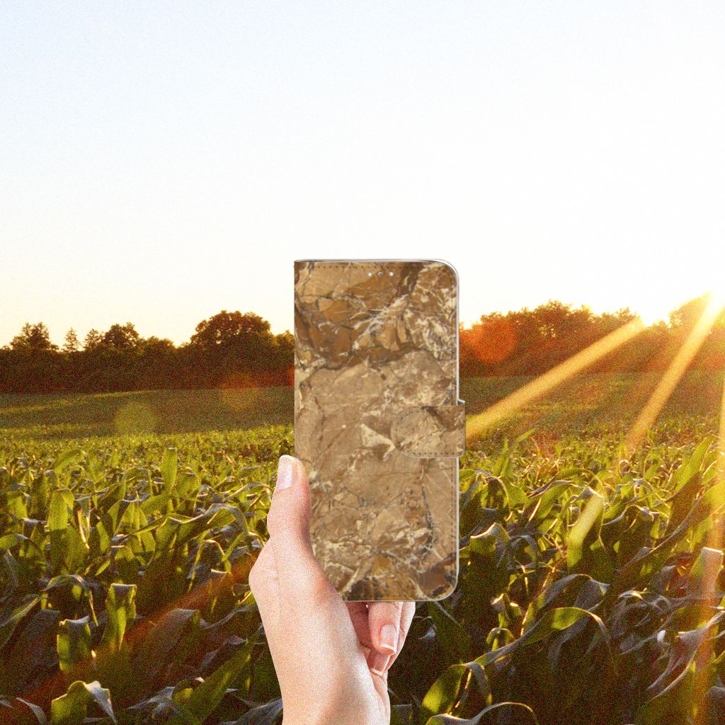 Samsung Galaxy A71 Bookcase Marmer Creme in hand against a sunset background over a green field.