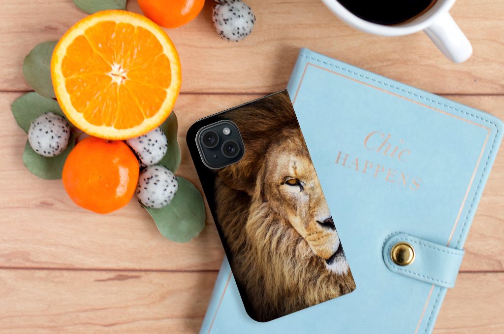 iPhone 15 Hoesje maken Leeuw met krachtige leeuw print, omgeven door vers fruit en een blauw notitieboekje.