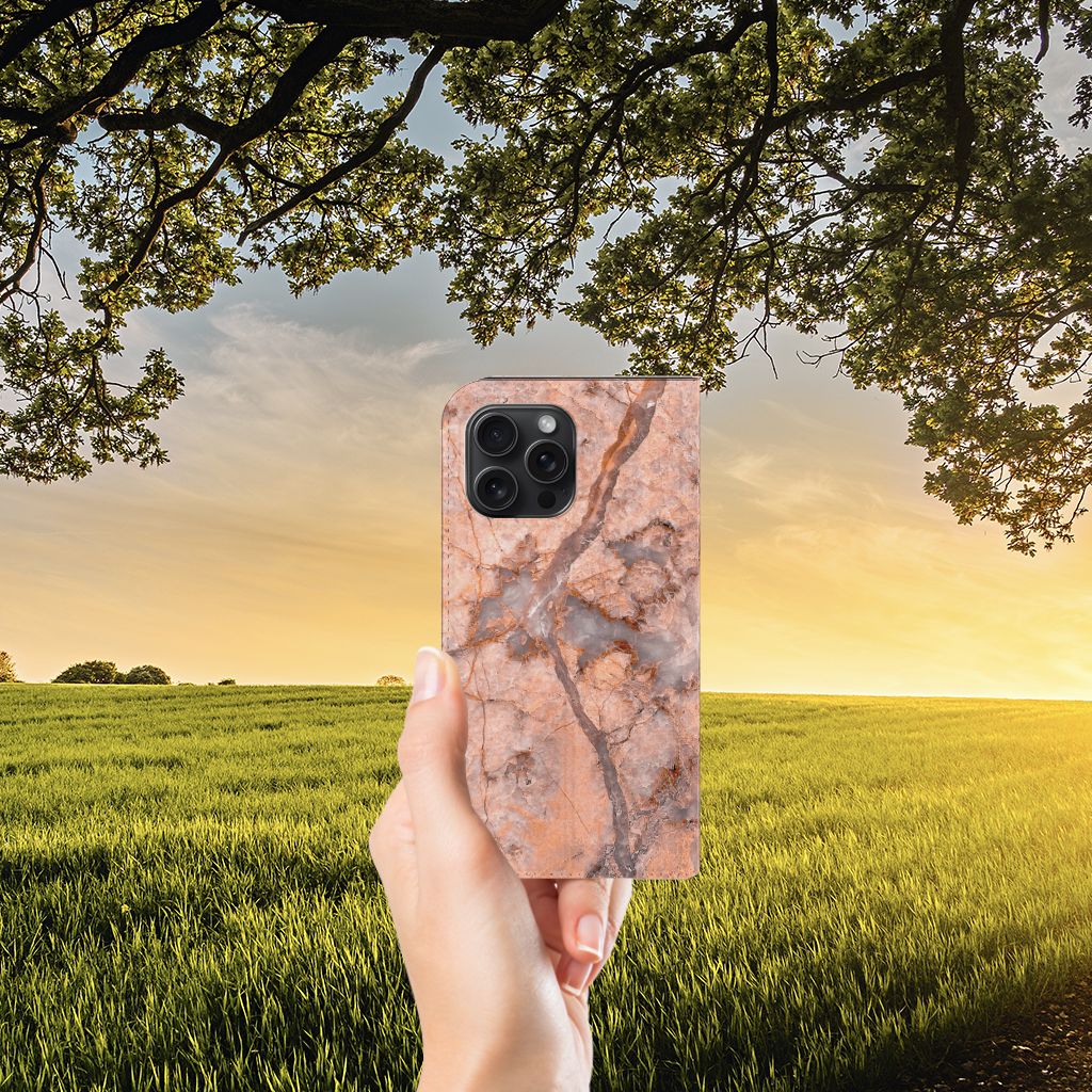 Hand holding an iPhone 15 Pro Max Standcase Marmer Oranje against a sunset backdrop.