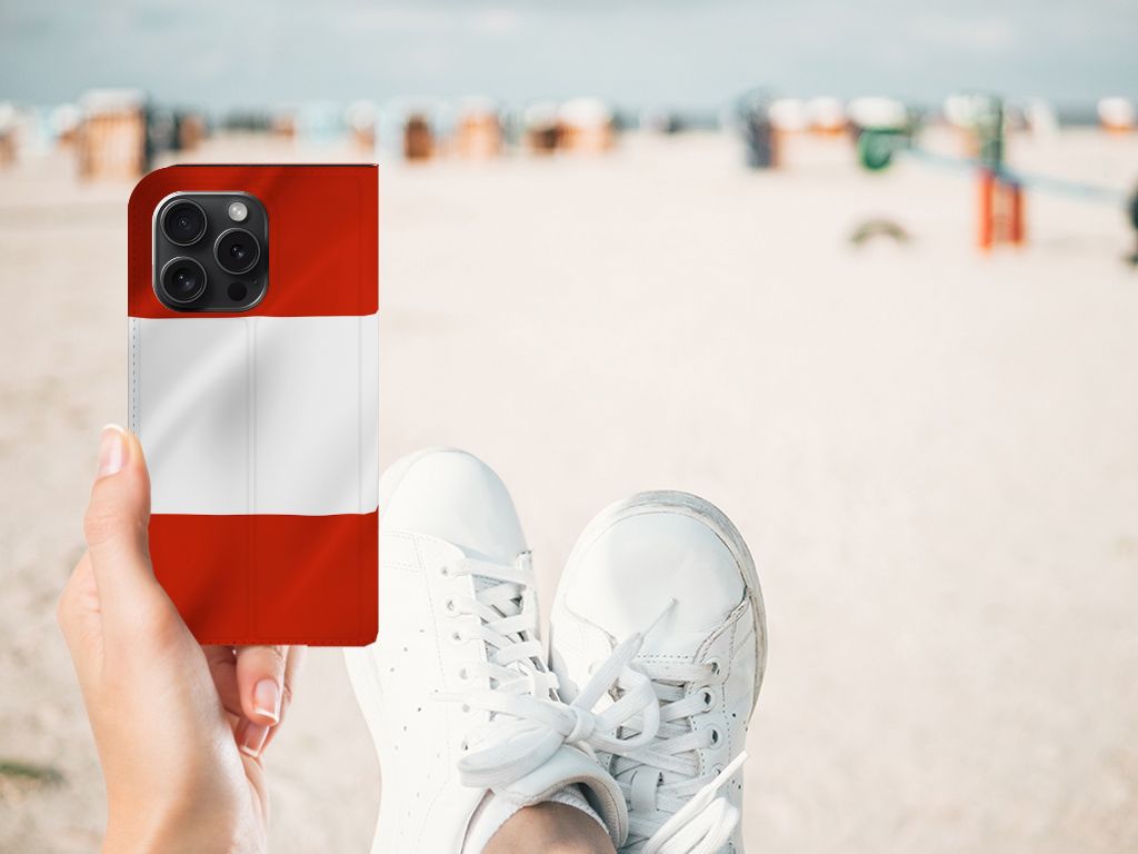 iPhone 15 Pro Standcase Oostenrijk met vlag, gehouden op het strand, casual sneakers zichtbaar.