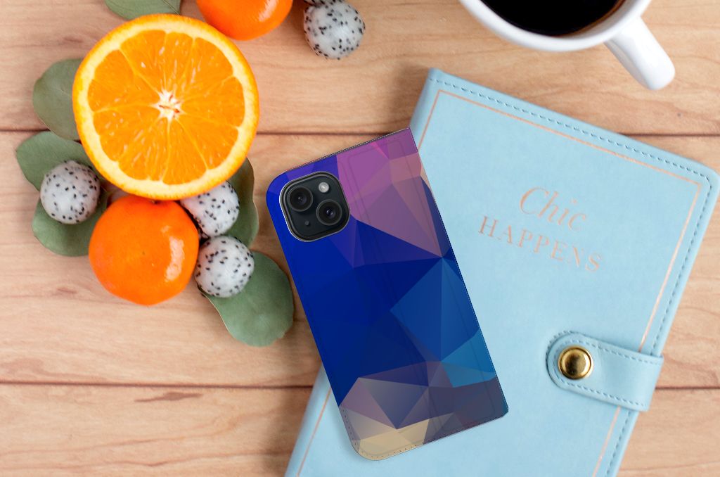 iPhone 15 Stand Case Polygon Dark met een abstract blauw en paarse motief, naast fruit en een notitieboekje. 🍊