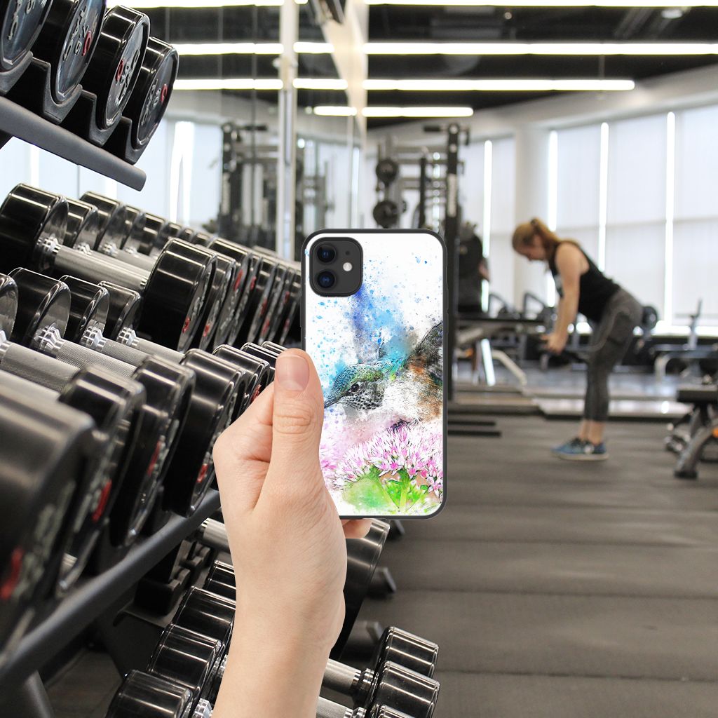 Kleurrijke Telefoonhoesje iPhone 11 Vogel in hand, afgebeeld in een sportschool met gewichten op de achtergrond.