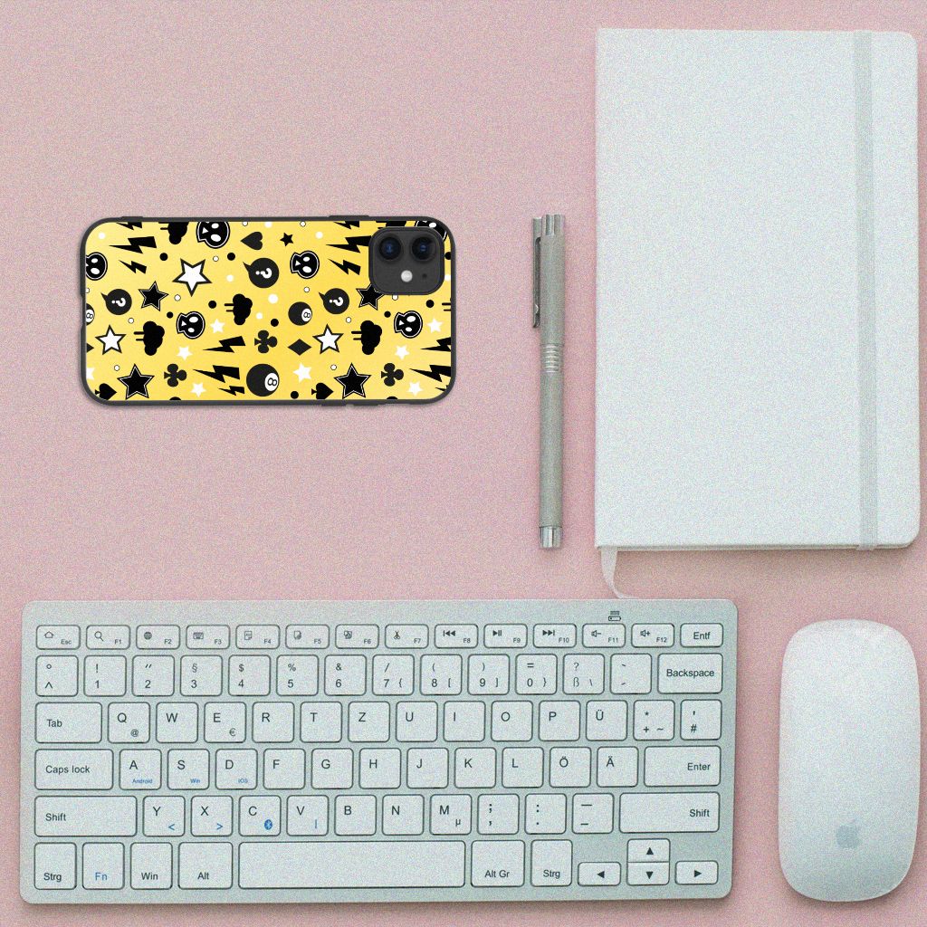 Telefoonhoesje iPhone 11 Punk Geel met felle skulls en sterren op een bureau met toetsenbord en notitieboek.