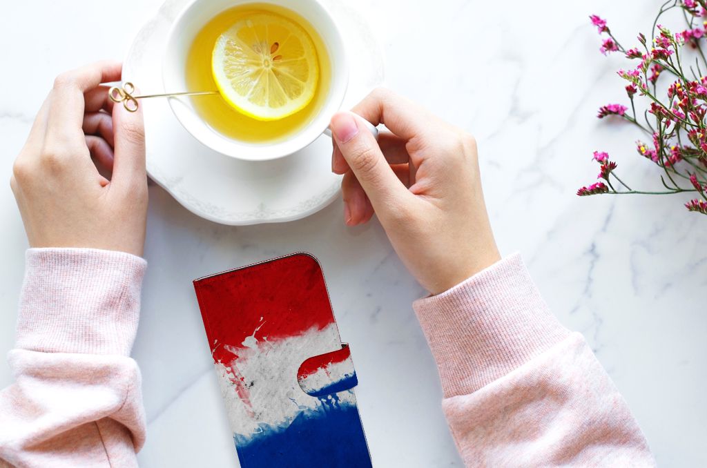 iPhone 15 Bookstyle Case Nederland naast een kop thee met citroen en bloemen op een marmeren tafel.