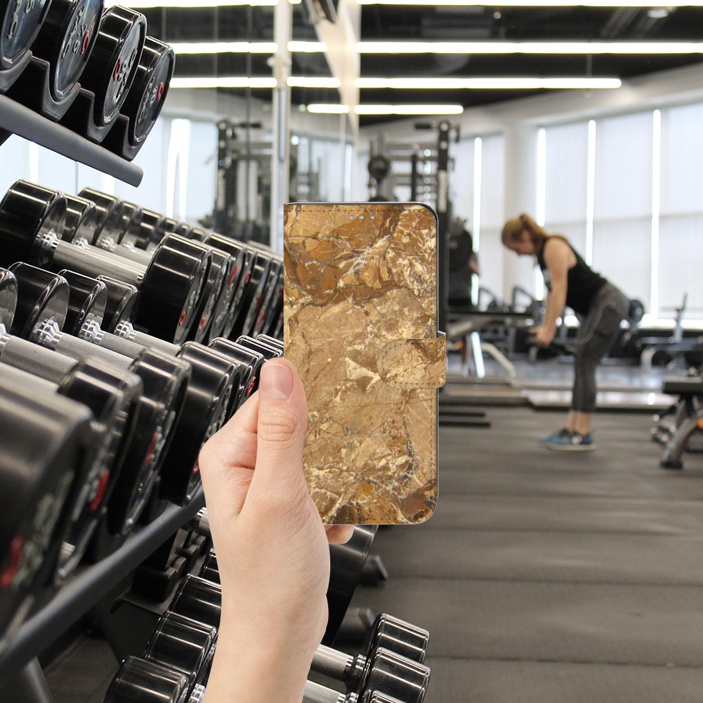Samsung Galaxy A21s Bookcase Marmer Creme met een luxe gouden marmerdesign in de hand in een sportschool.