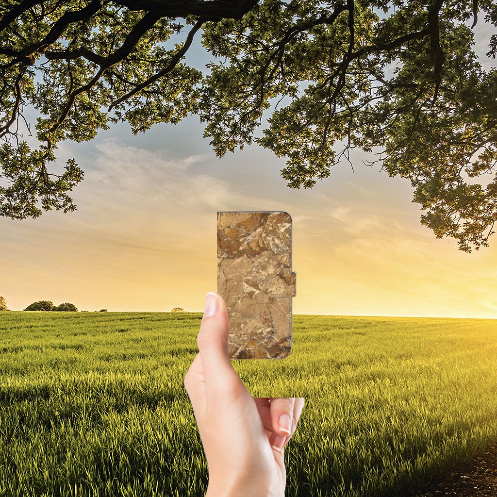 Samsung Galaxy A22 4G | M22 Bookcase Marmer Creme tegen een achtergrond van een zonsondergang en groene velden.