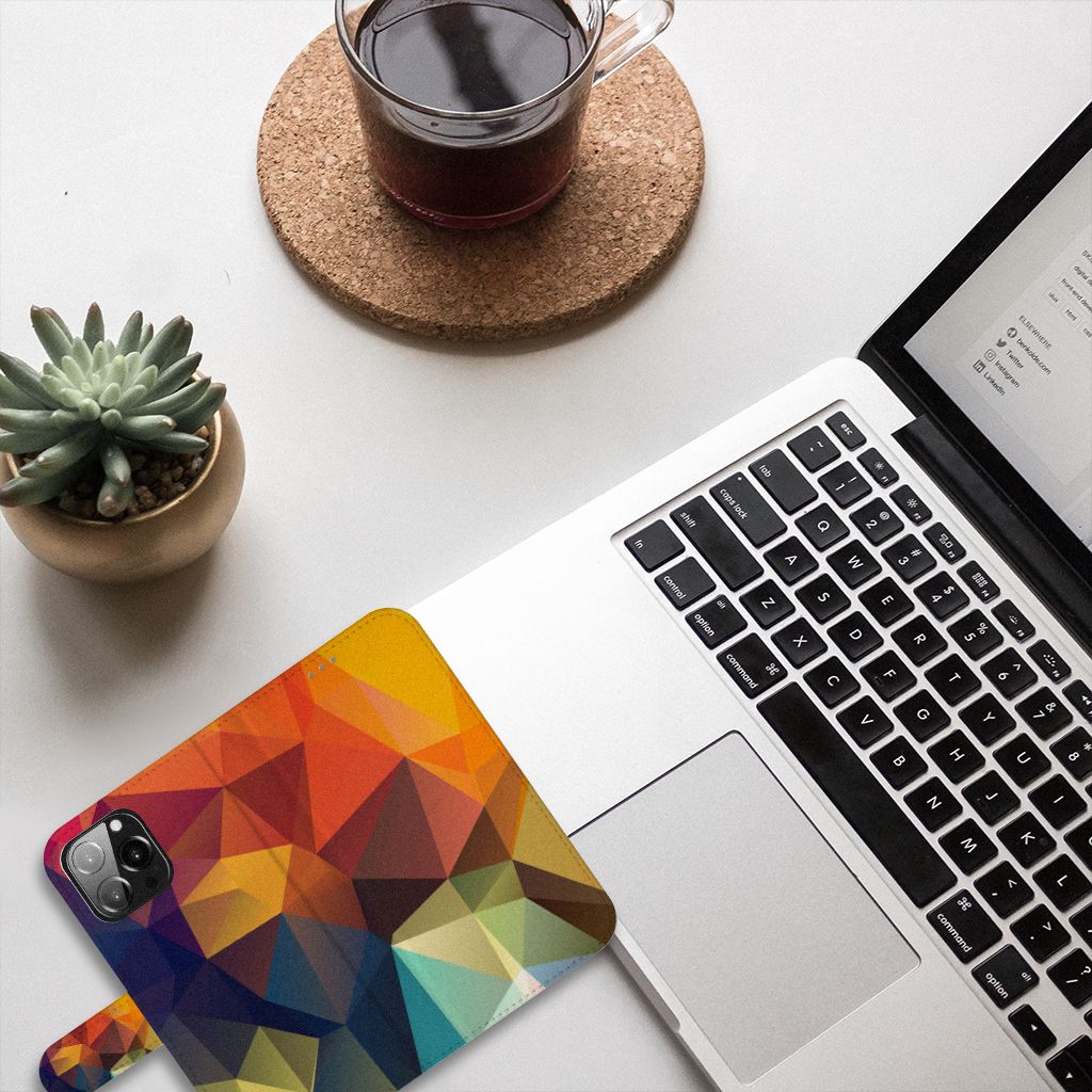 iPhone 13 Pro Max Book Case Polygon Color met kleurrijk geometrisch ontwerp, geplaatst op een bureau met een laptop en planten. 🌈