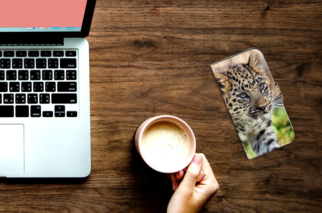 iPhone 15 Pro Telefoonhoesje met Pasjes Baby Luipaard ligt naast een laptop en een kop koffie.