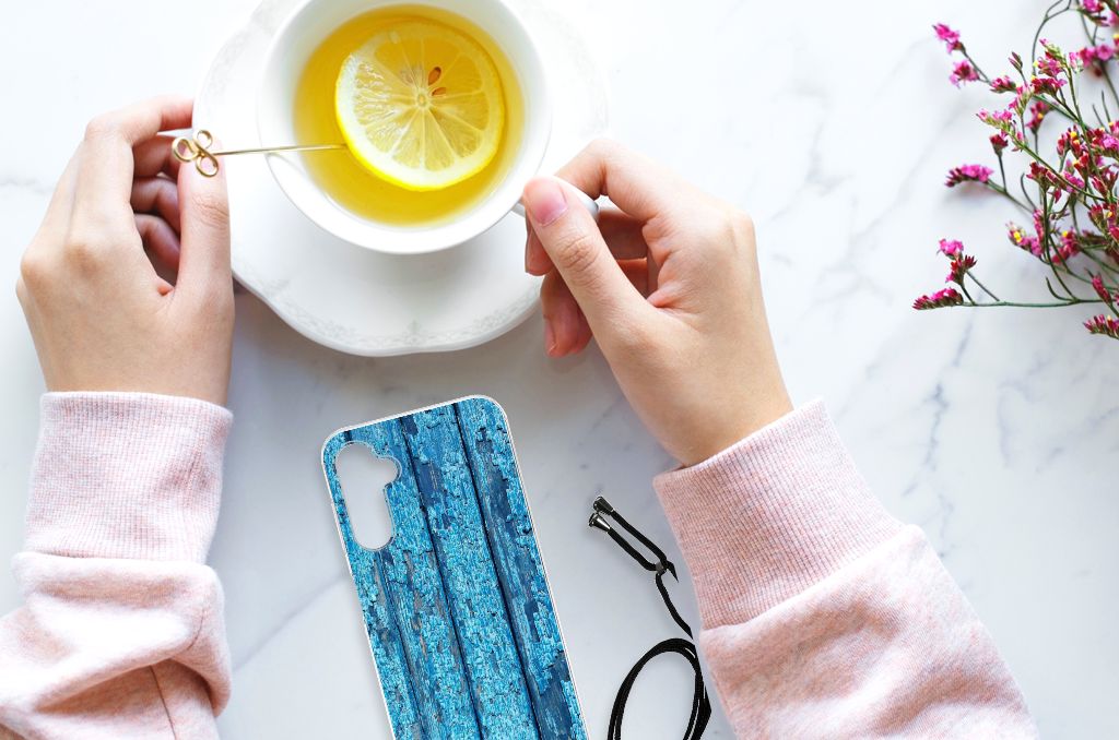 Persoon met een Samsung Galaxy A14 5G Stevig Telefoonhoesje Wood Blue naast een kopje thee met citroen.