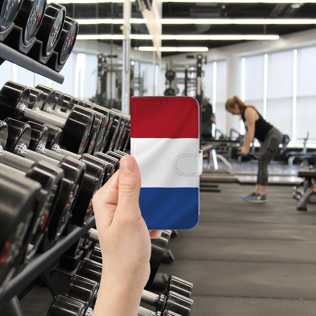 iPhone 13 Pro Bookstyle Case Nederlandse Vlag in hand, fitnessruimte met gewichten op de achtergrond.