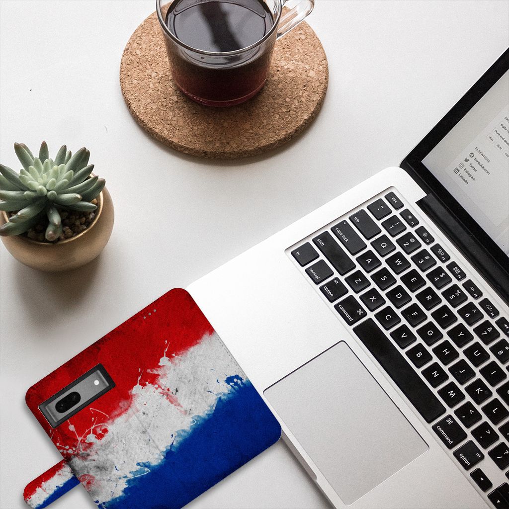 Google Pixel 7 Bookstyle Case Nederland naast een laptop met een kopje koffie en een plant op tafel.