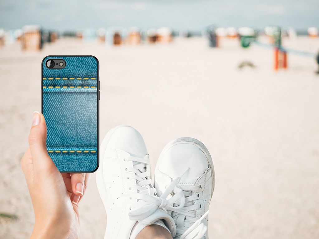 iPhone SE 2022 | SE 2020 | 7/8 GSM Cover Jeans held in hand with sneakers on sand beach background.