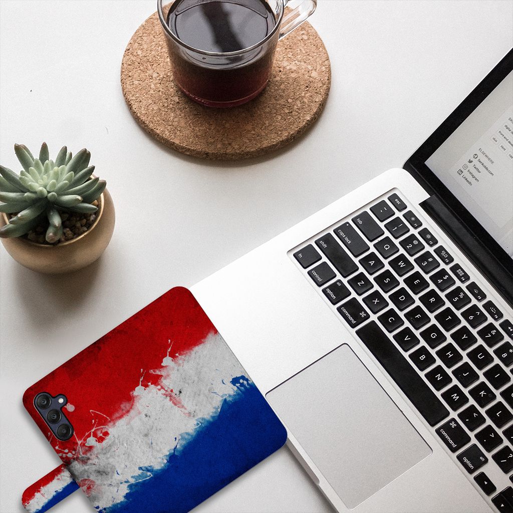 Samsung Galaxy A25 Bookstyle Case Nederland met artistiek design van de Nederlandse vlag op bureau met laptop.