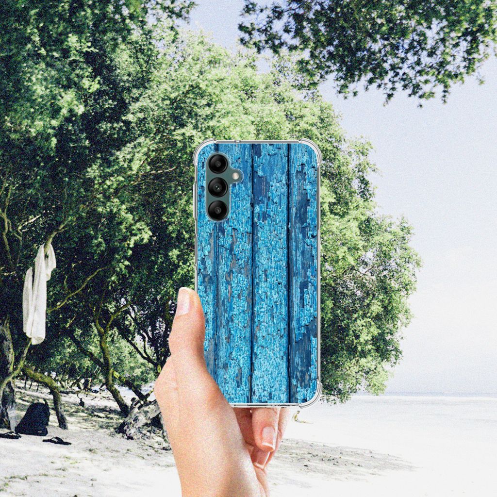 Samsung Galaxy A14 5G/4G Stevig Telefoonhoesje Wood Blue in hand op een strand met bomen op de achtergrond.