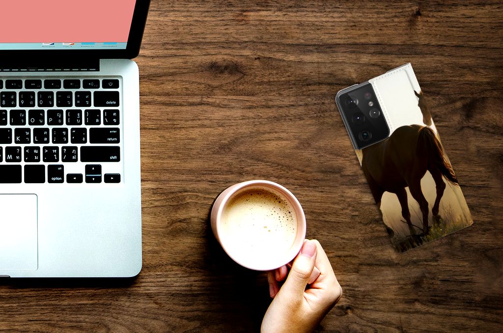 Samsung Galaxy S21 Ultra Hoesje maken Design Cowboy met paardenprint op een houten tafel naast een laptop en koffie.
