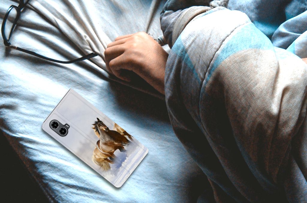 Motorola Moto G34 Hoesje maken Paarden met paard print op een bed naast een hand.