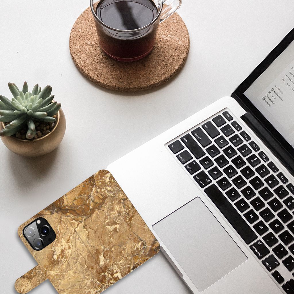 iPhone 14 Pro Bookcase Marmer Creme op een bureau met laptop en thee, luxe uitstraling en stevige bescherming.