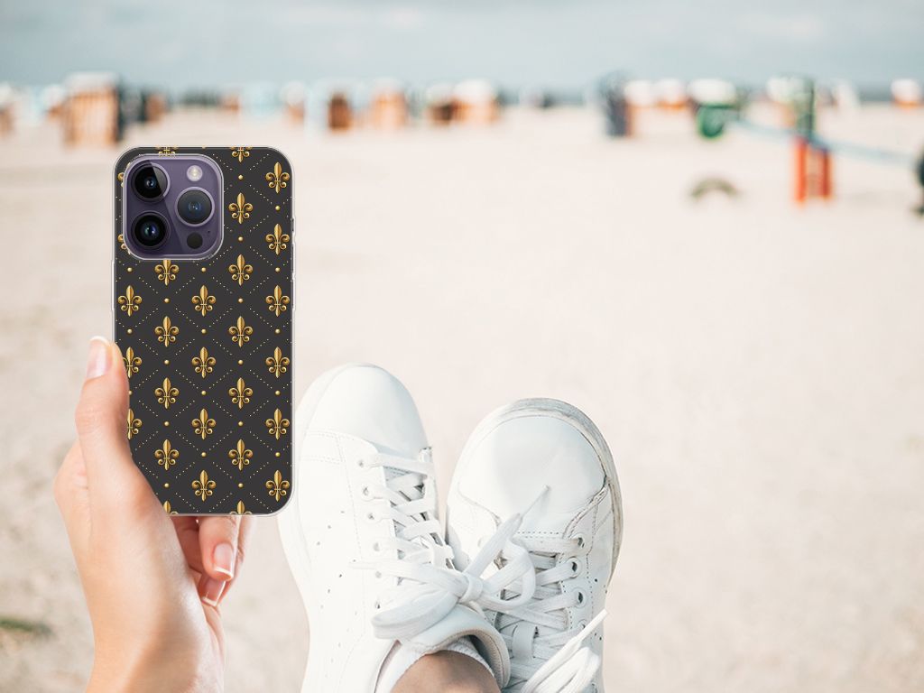 Apple iPhone 14 Pro TPU bumper Franse Lelie vastgehouden op het strand met witte sneakers.
