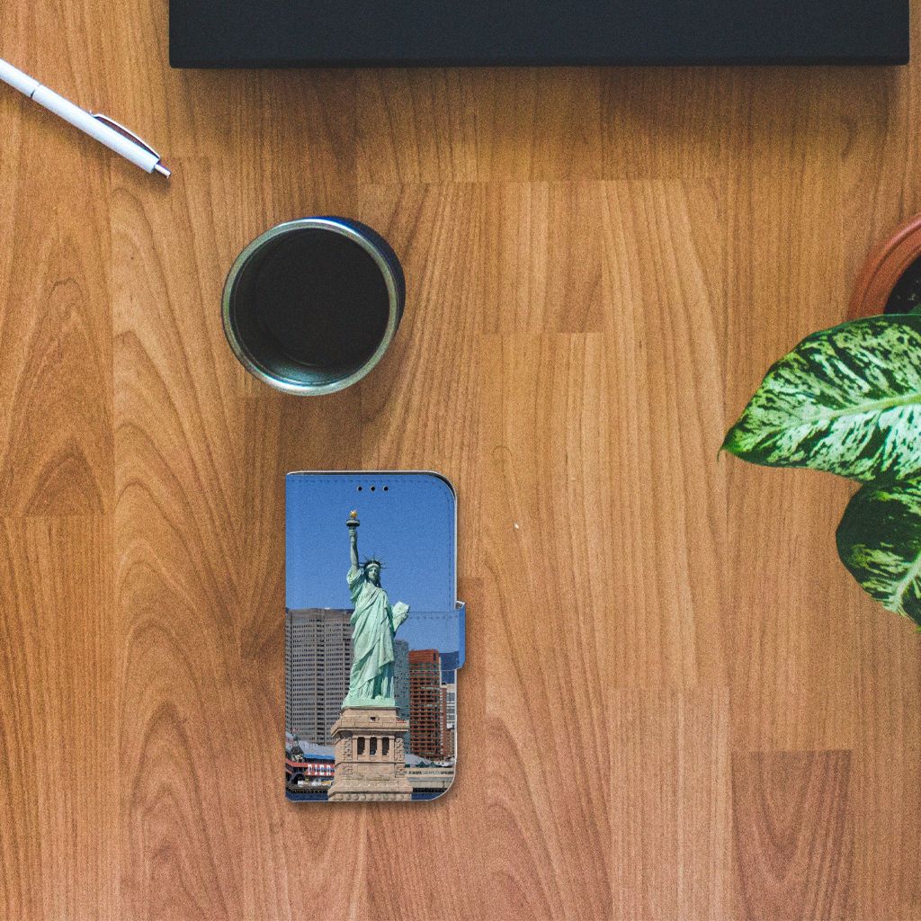 iPhone 13 Mini Flip Cover Vrijheidsbeeld met een afbeelding van het Vrijheidsbeeld op houten tafel met plant en koffie.