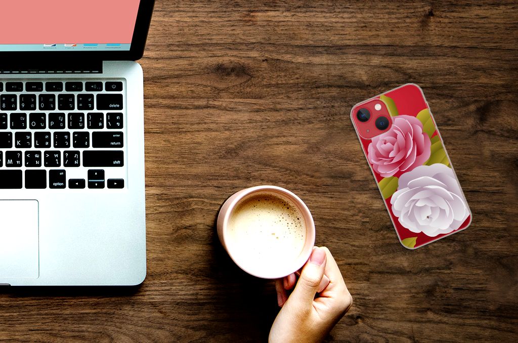 Apple iPhone 13 TPU Case Roses met roze bloemen ontwerpen ligt op een bureau naast een laptop en een kop koffie.