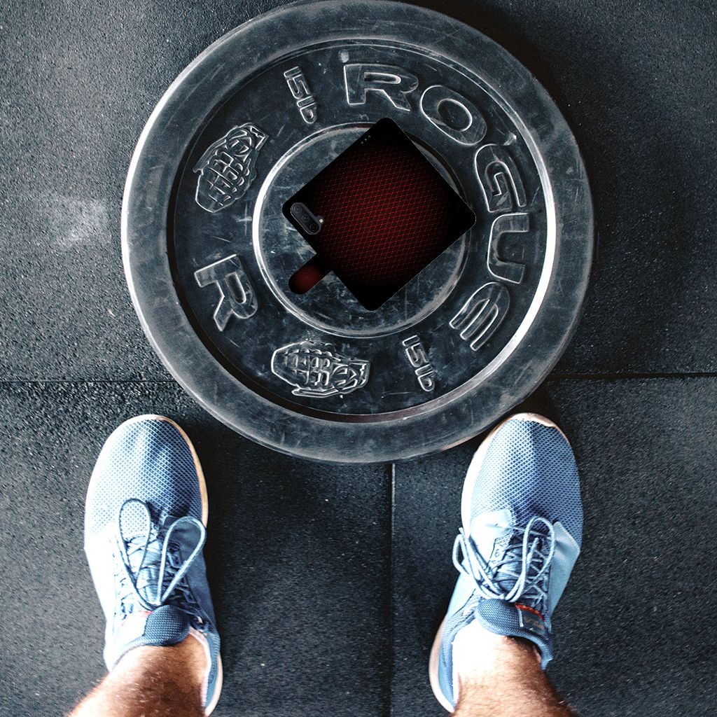 Persoon met blauwe sportschoenen staande boven een Rogue barringschijf op de vloer van een sportschool.