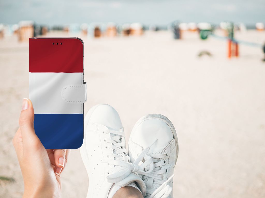 Huawei P20 Lite Bookstyle Case Nederlandse Vlag in hand, met sneakers aan op het strand.
