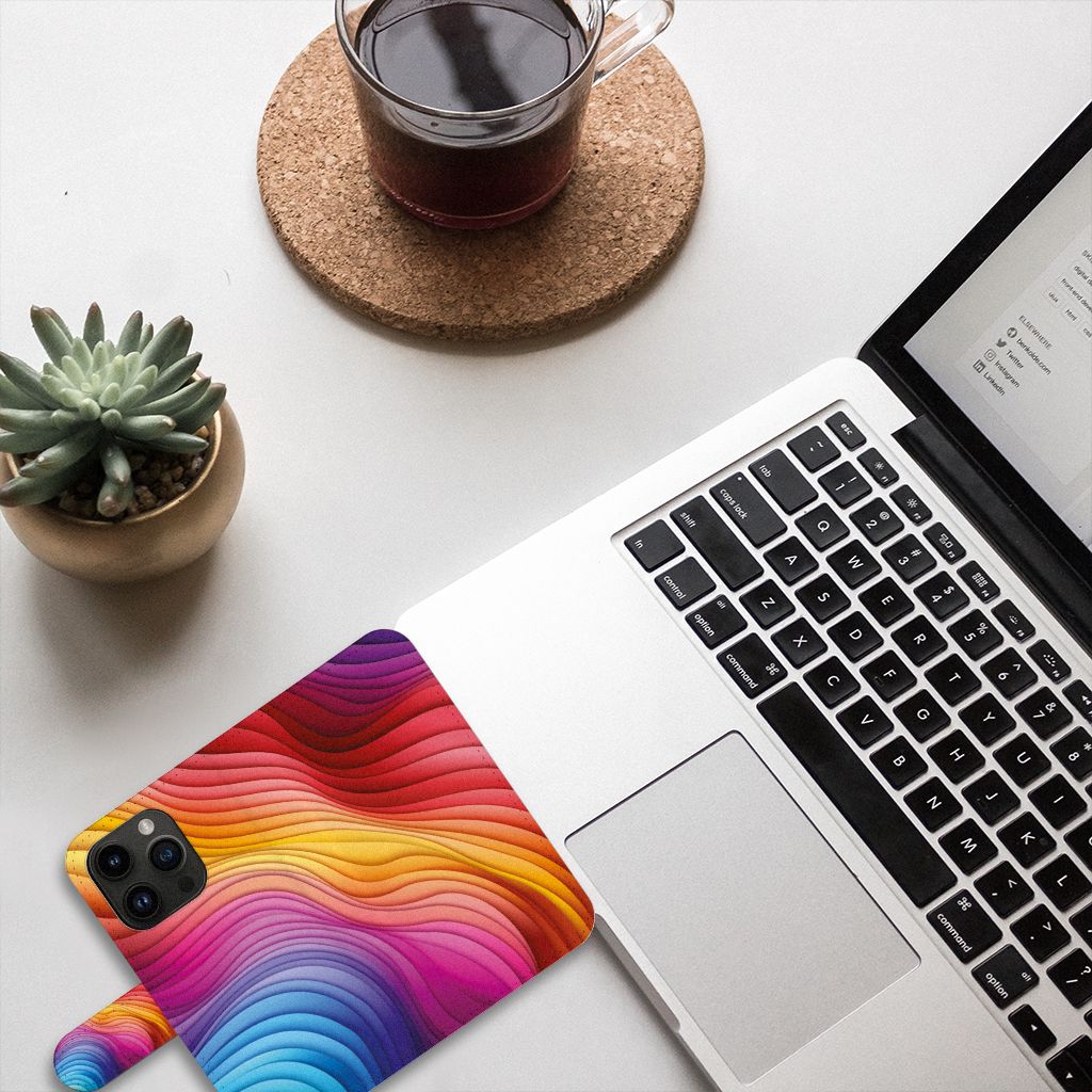 Book Case voor iPhone 15 Pro Regenboog met kleurrijk ontwerp op een bureau met laptop en planten.